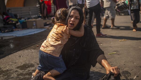 پناهنده ای با دختری که پس از استفاده از گاز اشک آور توسط مقامات یونانی در درگیری در نزدیکی شهر میتیلینی در جزیره لسوس پاکسازی شد - اسپوتنیک ایران  