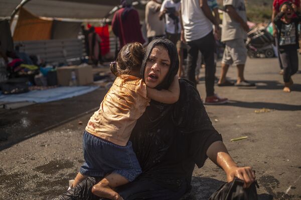 پناهنده ای با دختری که پس از استفاده از گاز اشک آور توسط مقامات یونانی در درگیری در نزدیکی شهر میتیلینی در جزیره لسوس پاکسازی شد - اسپوتنیک ایران  