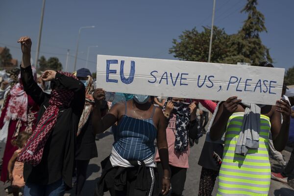 مهاجران در تظاهرات در نزدیکی شهر میتیلینی در جزیره لسوس، یونان با پرچم اتحادیه اروپا ما را نجات دهید در دست دارند. - اسپوتنیک ایران  