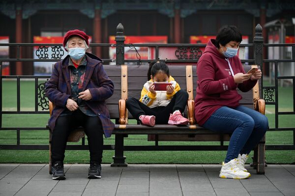 دختری در حالی که روی نیمکتی در پکن استراحت می کند از تلفن همراه استفاده می کند. - اسپوتنیک ایران  
