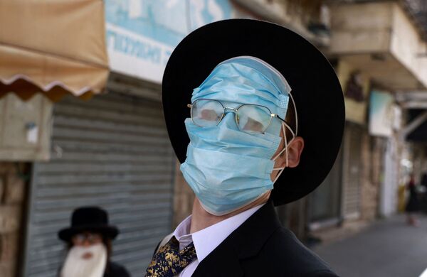 مردی هنگام برگزاری جشن های پوریم در اورشلیم چندین  ماسک محافظتی بر صورتش گذاشته. - اسپوتنیک ایران  