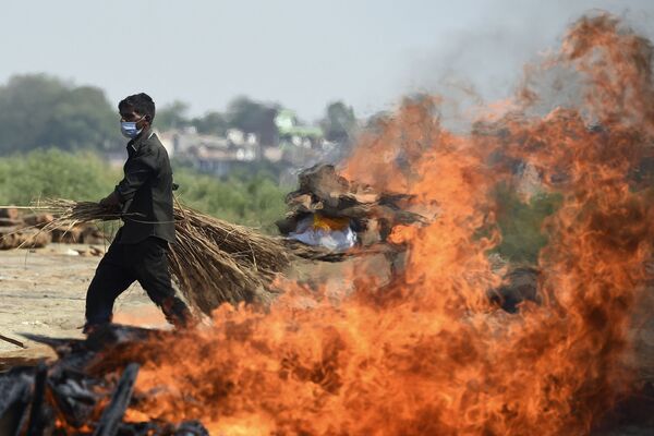 عبور کارگری از کنار آتش برخاسته از سوزاندن اجساد مبتلا به ویروس کرونا در هند  - اسپوتنیک ایران  