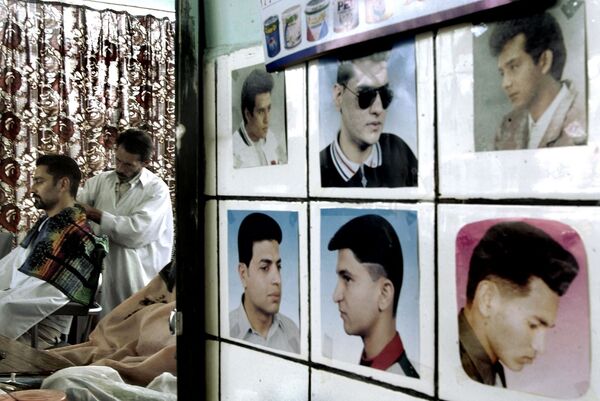 در یک آرایشگاهی در کابل سال ۲۰۰۲، عکس هایی روی دیوار آویزان شده است که سبک های مختلف موهای بدون ریش را نشان می دهد - اسپوتنیک ایران  