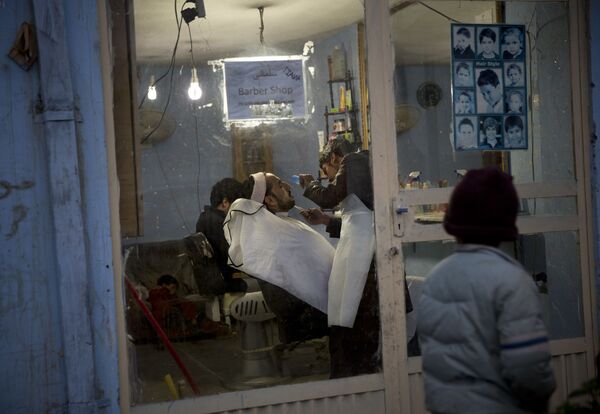 پسری به آرایشگاهی در کابل سال ۲۰۱۳ نگاه می کند که در آن ریش مردی در حال کوتاه شدن است - اسپوتنیک ایران  
