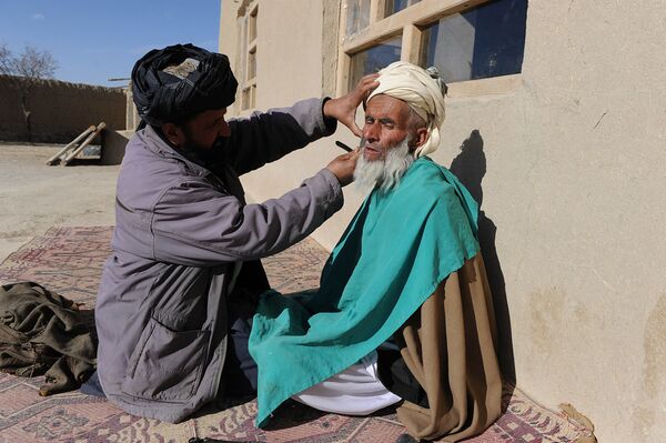 آرایشگر روستایی در حال زدن ریش مردی در ولایت غزنی افغانستان در سال ۲۰۱۱ - اسپوتنیک ایران  