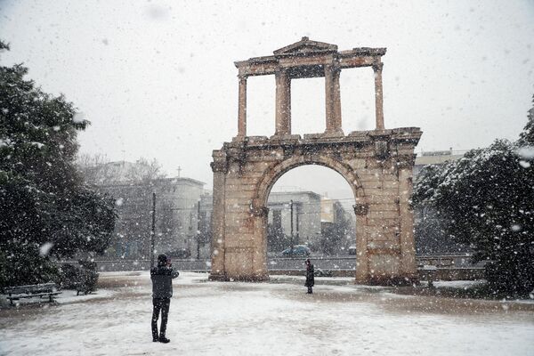 مردم از برف کنار دروازه هادریان، در جریان بارش شدید برف در آتن یونان، ۲۴ ژانویه ۲۰۲۲ عکس می گیرند. - اسپوتنیک ایران  