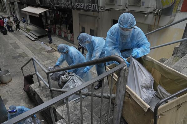 کارمندان در لباس های ایمنی در حال جمع‌آوری کیسه های زباله و بیرون بردن آن ها از هتلی متروک در هنگ کنگ. - اسپوتنیک ایران  