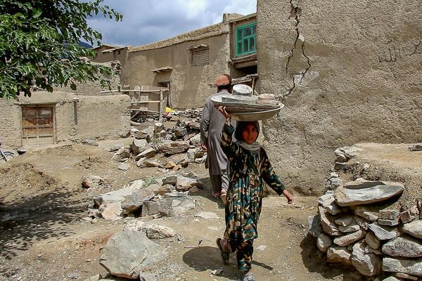 پس از زلزله در ولسوالی گایان، استان پکتیکا در ۲۲ ژوئن ۲۰۲۲، کودکی که ظروف بر سر خود حمل می کند، از کنار خانه های آسیب دیده عبور می کند. - اسپوتنیک ایران  