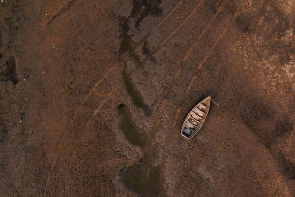 نمای هوایی از ردهای یک وسیله نقلیه در بستر رودخانه در کنار یک قایق سرگردان در رودخانه خشک پارانا، که سطح آب آن به پایین ترین سطح تاریخی رسیده است، در طول یک خشکسالی تاریخی در گویا، کورینتس، آرژانتین، 21 اوت 2021 - اسپوتنیک ایران  