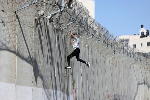 جوانی پس از صعود و عبور از روستای الرام در 11 ژوئیه 2022، با طناب از دیوار بتنی دیوار جدایی جنجالی اسرائیل به سمت محله بیت حنینه شرقی اورشلیم فرود می آید - اسپوتنیک ایران  