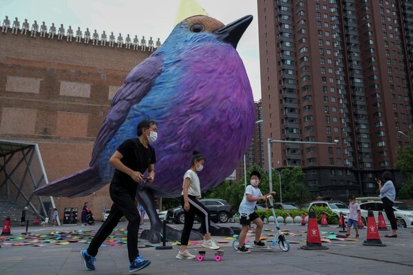 ساکنانی که ماسک بر چهره دارند از کنار یک سازه پرنده غول پیکر که در بیرون یک گالری هنری در پکن به نمایش گذاشته شده است، عبور می کنند. - اسپوتنیک ایران  