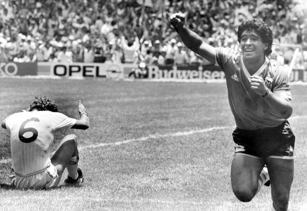 دیگو مارادونای آرژانتینی پس از اینکه دومین گل خود را در یک چهارم نهایی جام جهانی در مکزیکو سیتی مکزیک در 22 ژوئن 1986 به ثمر رساند، در زمین فوتبال با خوشحالی می دود. تری بوچر از انگلیس روی زمین نشسته است. - اسپوتنیک ایران  
