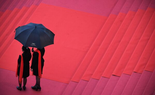 مهمانداران در حالی که در 16 مه 2018 روی فرش قرمز زیر باران منتظر می مانند، چتر در دست دارند و قبل از نمایش فیلم &quot;سوختن&quot; در هفتاد و یکمین دوره جشنواره فیلم کن در کن، جنوب فرانسه. - اسپوتنیک ایران  