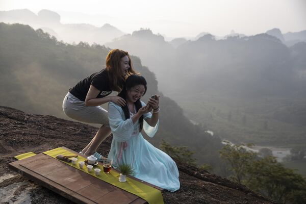 دختران در روز چهارشنبه، 14 آگوست 2019، بر روی یک عکس برای تبلیغ محصولات چای خود بر روی قله کوهی  در استان فوجیان در شرق چین کار می کنند.  - اسپوتنیک ایران  
