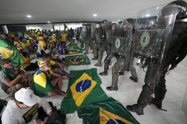 معترضان، حامیان ژائیر بولسونارو، رئیس جمهور سابق برزیل، پس از هجوم به کاخ پلانالتو در برازیلیا، در مقابل پلیس نشسته اند. - اسپوتنیک ایران  