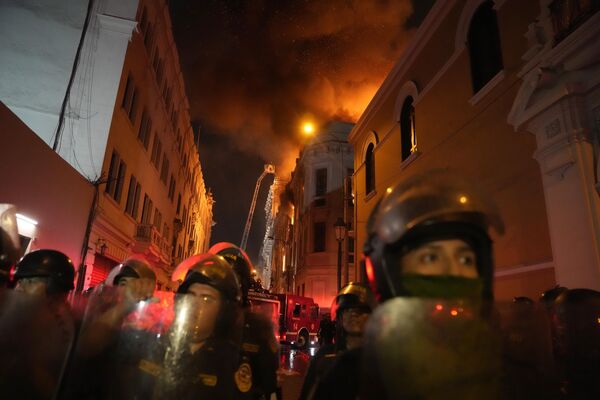 پس از یک روز درگیری با معترضان ضد دولتی در لیما، پرو، روز  پنجشنبه، 19 ژانویه 2023  پلیس با تجهیزات ضد شورش به علت آتش گرفتن ساختمان پشت سر آنها خیابان رامسدود کرد. - اسپوتنیک ایران  