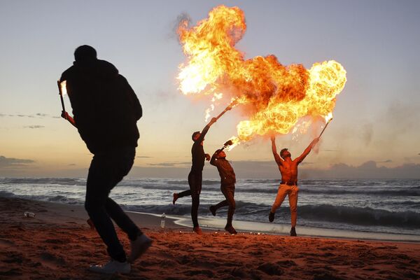 جوانان فلسطینی در 13 ژانویه 2023 مهارت های تنفس آتشین خود را در کنار ساحل شهر غزه نشان می دهند. (عکس از Mohammed ABED / AFP) - اسپوتنیک ایران  