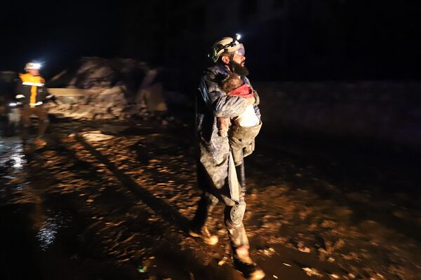 یکی از اعضای دفاع مدنی سوریه، معروف به کلاه سفیدها، کودکی را حمل می کند که پس از زلزله 6 فوریه در شهر زردان در حومه شمال غربی ادلب سوریه از زیر آوار نجات یافته است. - اسپوتنیک ایران  