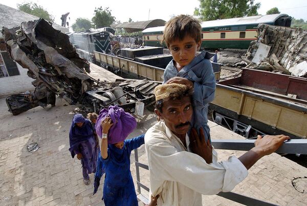 یک مرد پاکستانی خانواده خود را از کنار لاشه واگن های قطار در گوتکی، در حدود 430 کیلومتری شمال شرق کراچی عبور می دهد. در این حادثه که مرگبارترین حادثه ریلی در پاکستان بود، 150 نفر کشته شدند.14 ژوئیه 2004 - اسپوتنیک ایران  