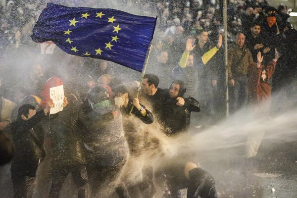معترضان در 7 مارس 2023 در نزدیکی پارلمان گرجستان در تفلیس در جریان درگیری با پلیس ضد شورش  پرچم اتحادیه اروپا را به اهتزاز در می‌آورند.پلیس گرجستان روز سه شنبه در حالی که هزاران تظاهرکننده در پایتخت تفلیس برای مخالفت با لایحه جنجالی &quot;عوامل خارجی&quot; به خیابان ها آمدند، از گاز اشک آور و ماشین آبپاش علیه معترضان استفاده کرد. - اسپوتنیک ایران  