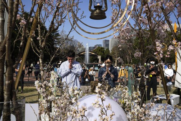  مرد و  زنی پس از گذاشتن گل در مقابل بنای یادبود قربانیان  دوازدهمین سالگرد زلزله عظیم، سونامی و فاجعه هسته‌ای در پارک هیبیا در توکیو، دعا می‌کنند. - اسپوتنیک ایران  