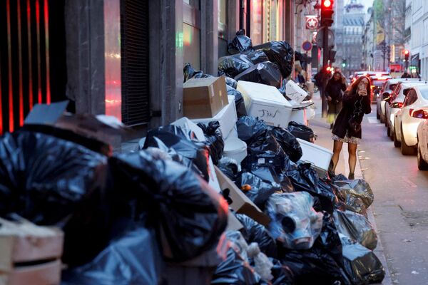 یک زن از انبوه کیسه‌های زباله که از زمان اعتصاب  کارگران جمع‌آوری زباله علیه اصلاحات پیشنهادی دولت فرانسه در حقوق بازنشستگی در پاریس در 20 مارس 2023 در حال انباشته شدن بوده است، عکس می‌گیرد.  - اسپوتنیک ایران  