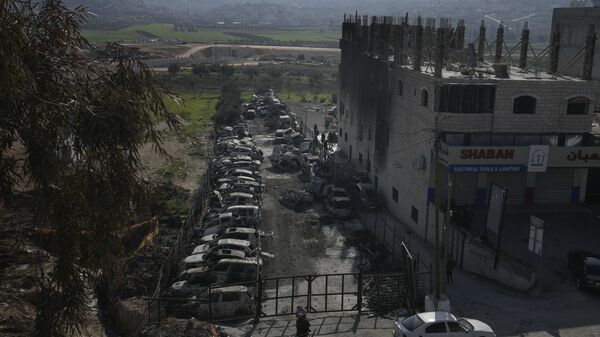 Палестинцы смотрят на сожженные автомобили и поврежденное здание в городе Хавара, недалеко от города Наблус на Западном берегу - اسپوتنیک ایران  