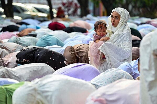 یک زن مسلمان در مراسم  نماز عید فطر  در مجتمع دانشگاه محمدیه در باندا آچه در 21 آوریل 2023، در حال مراقبت از یک کودک است. - اسپوتنیک ایران  