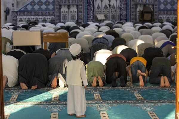 پسری به نمازگزاران مسلمان سنی در روز  عید فطر، که  در مسجد جامع بصره در 21 آوریل 2023 نماز می خوانند، نگاه می کند. - اسپوتنیک ایران  