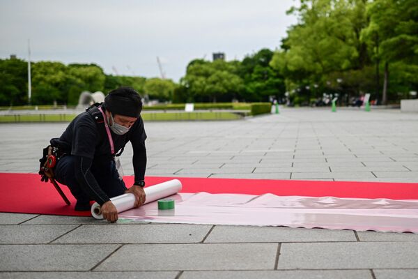 هنگامی که رهبران برای شرکت در نشست سران کشورهای گروه هفت در هیروشیما به شهر می‌رسند، مردی به پهن کردن فرش قرمز در پارک یادبود صلح کمک می‌کند. - اسپوتنیک ایران  