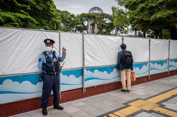 در حالی که یک افسر پلیس در خارج از پارک یادبود صلح در هیروشیما نگهبانی می‌دهد، مردی  به داخل پارک نگاه می‌کند. - اسپوتنیک ایران  