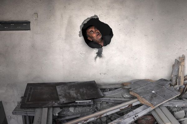 مردی در 13 مه 2023 از سوراخی در میان آوارهای ساختمانی که در جریان  حمله هوایی اسرائیل در دیرالبلاح در مرکز نوار غزه مورد اصابت قرار گرفته است نگاه می کند. - اسپوتنیک ایران  