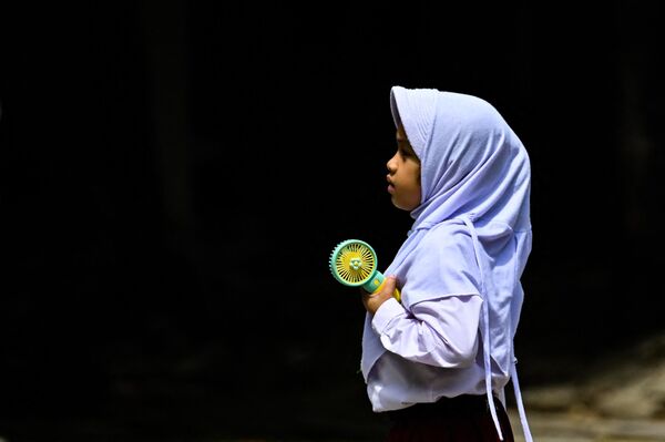 یک دانش آموز دبستانی از یک پنکه قابل حمل برای خنک ماندن در هوای گرم در شهر باندا آچه اندونزی استفاده می کند - اسپوتنیک ایران  