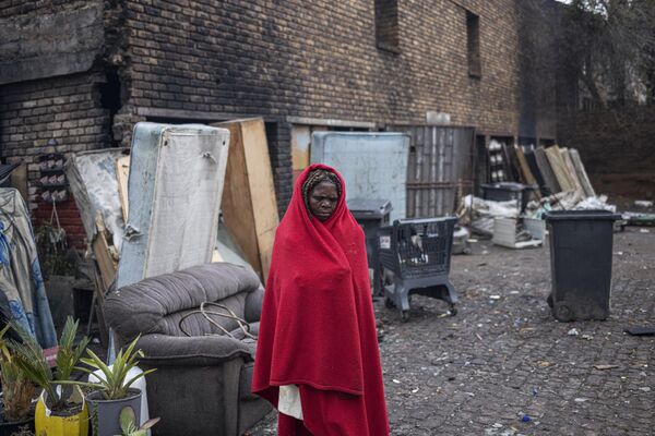 زنی در ژوهانسبورگ آفریقای جنوبی در کنار ساختمانی مخروبه که به عنوان سرپناه استفاده می شود خود را با پتویی می پوشاند. - اسپوتنیک ایران  