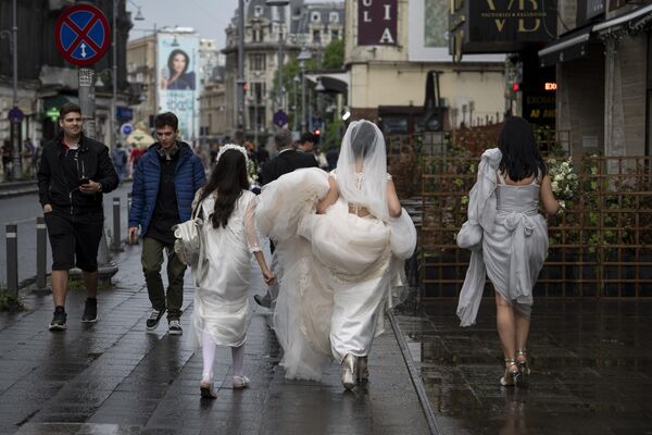 عروس بعد از بارندگی در مرکز شهر بخارست، رومانی  لباس خود را حمل می کند، - اسپوتنیک ایران  