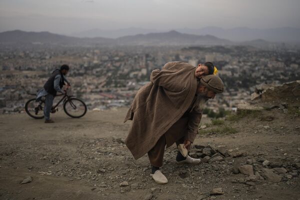 عبدالقادر قاضی زاده، 61 ساله، در حالی که پسرش احمد سر، 2 ساله را حمل می کند، سنگ ها را از جاده می کند تا دوچرخه ها و اتومبیل ها  در کابل بهتر تردد کنند. - اسپوتنیک ایران  