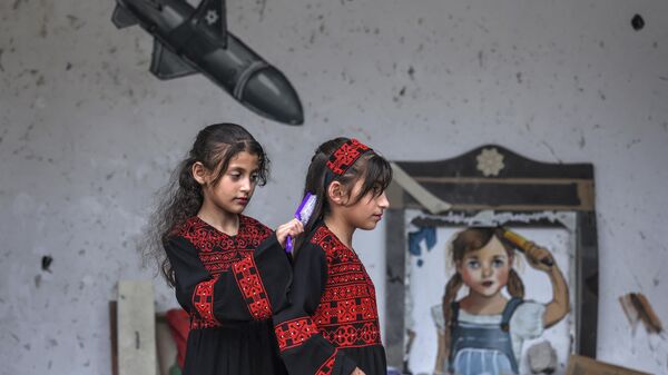 Палестинская девочка расчесывает волосы другой перед фреской во время выставки под названием Oккупация убивает детство в Газе, Палестина - اسپوتنیک ایران  
