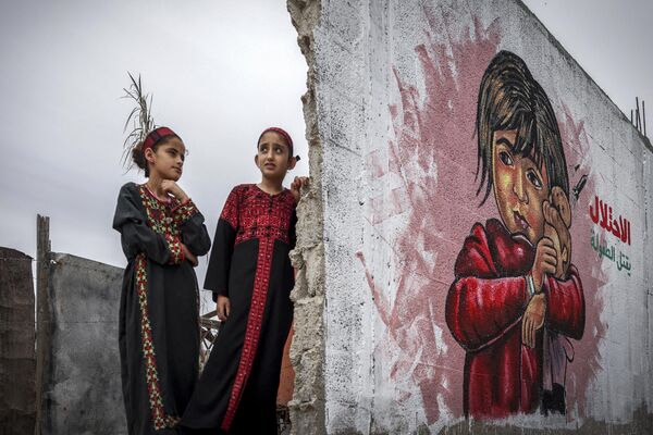 کودکان فلسطینی در نمایشگاه هنری  با عنوان &quot;اشغال کودکی را می کشد&quot; با نقاشی دیواری ژست می گیرند. - اسپوتنیک ایران  