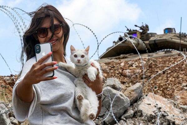 یک زن  با گربه اش در امتداد حصار سیم خاردار که خط آبی را مشخص می کند  که توسط سازمان ملل متحد برای نشان دادن خروج اسرائیل از جنوب لبنان در سال 2000 ترسیم شده است، سلفی می گیرد.  11 ژوئن 2023. - اسپوتنیک ایران  