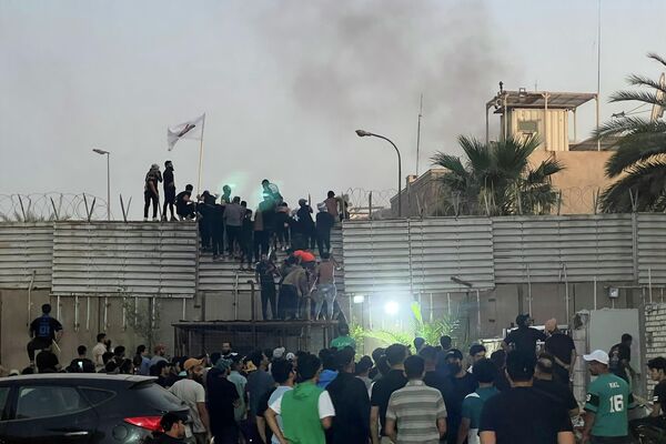 معترضان  از دیوار سفارت سوئد در بغداد بالا می روند. - اسپوتنیک ایران  