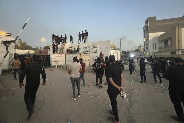 معترضان  از دیوار سفارت سوئد در بغداد بالا رفته اند. - اسپوتنیک ایران  