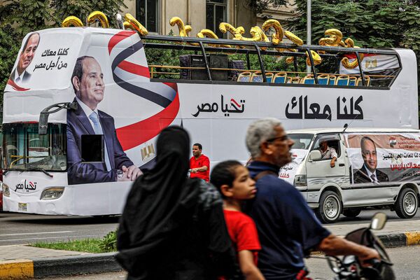 مرد، کودک و زن سوار بر موتورسیکلت از کنار اتوبوسی برای تبلیغات انتخاباتی عبدالفتاح السیسی، رئیس جمهور مصر که به تصویر و شعار او 