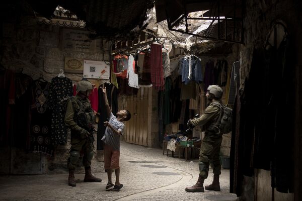 یک کودک فلسطینی در حالی که سربازان اسرائیلی در بازار سرپوشیده شهر الخلیل کرانه باختری در روز سه‌شنبه، 3 اکتبر 2023، در تعطیلات هفته‌ای سوکوت، برای بزرگداشت 40 سال سرگردانی اسرائیلی‌ها در صحرا، نگهبانی می‌دهند، با تیله بازی می‌کند - اسپوتنیک ایران  