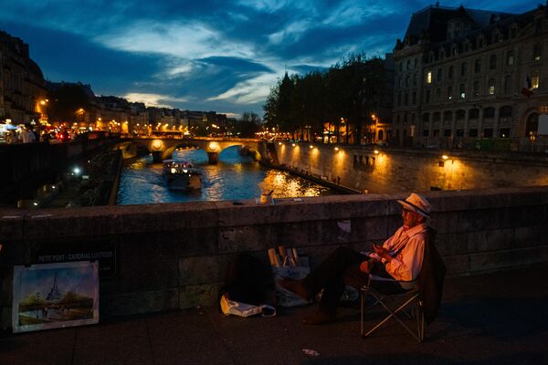 یک هنرمند نقاشی های خود را در شب در پل پتی پونت در پاریس در 2 اکتبر 2023 می فروشد - اسپوتنیک ایران  
