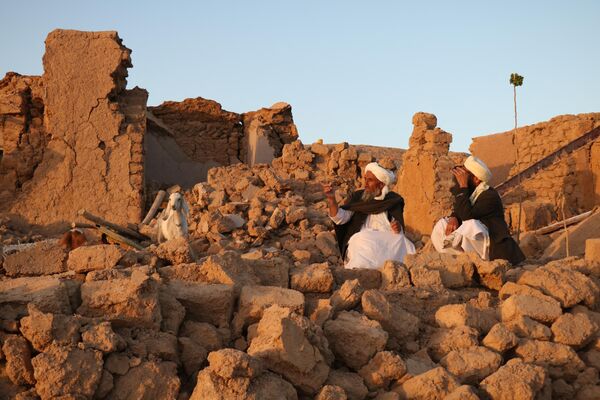 نشستن اهالی افغان در یک خانه آسیب دیده پس از زلزله در روستای سربلند زنده جان ولسوالی هرات، روز شنبه 7 اکتبر 2023 (Photo by Mohsen KARIMI / AFP) - اسپوتنیک ایران  