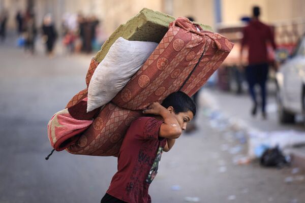 پس از حمله هوایی اسرائیل در 13 اکتبر 2023، در  شرایطی که فلسطینی‌ها با وسایلشان به مناطق امن‌تر در شهر غزه فرار می‌کنند، پسری تشک را حمل می‌کند. اسرائیل خواستار جابجایی فوری 1.1 میلیون نفر در غزه در بحبوحه بمباران گسترده‌اش در تلافی حملات حماس شده است.  سازمان ملل در مورد عواقب &quot;ویرانگر&quot; این کار به اسرائیل هشدار داده است. - اسپوتنیک ایران  