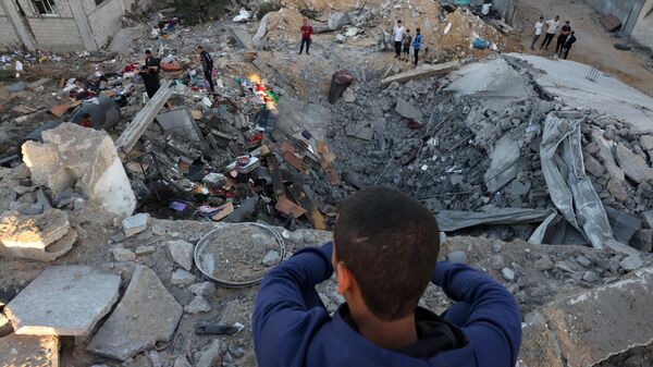 Мальчик наблюдает, как люди разбирают обломки здания, разрушенного в результате израильской бомбардировки в Рафахе на юге сектора Газа - اسپوتنیک ایران  