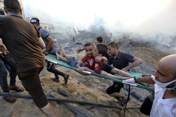 فلسطينی ها دو پسر زخمی را از زير خانه های ويران شده در اثر حمله هوايی اسرائيلی به غزه خارج می کنند. - اسپوتنیک ایران  