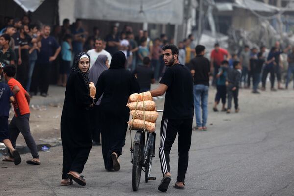 مردی در پی حملات اسرائیل به شهر غزه در 28 اکتبر 2023 کیسه های غذا را با دوچرخه حمل می کند. حملات هوایی اسرائیل صدها ساختمان را در نوار غزه یک شبه ویران کرد. - اسپوتنیک ایران  