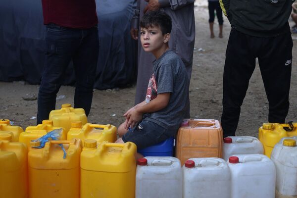 یک جوان فلسطینی در بحبوحه نبردهای جاری بین اسرائیل و گروه فلسطینی حماس، روی قوطی های پلاستیکی در نقطه پر کردن آب، در رفح در جنوب نوار غزه نشسته است.  - اسپوتنیک ایران  